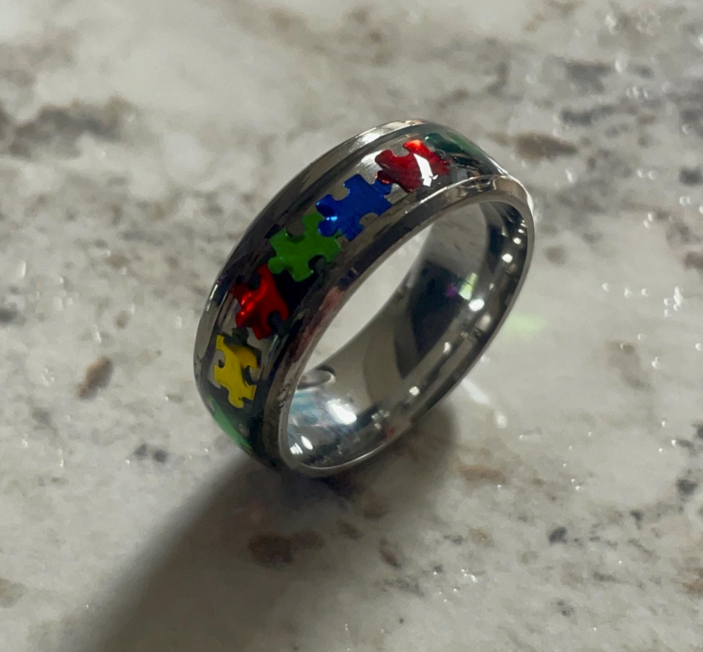 A stainless steel epoxy ring with puzzle piece inlays, symbolizing the beauty and strength of neurodiversity.